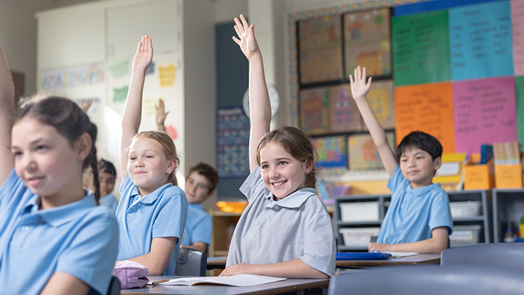 school children in a classroom with their hand up