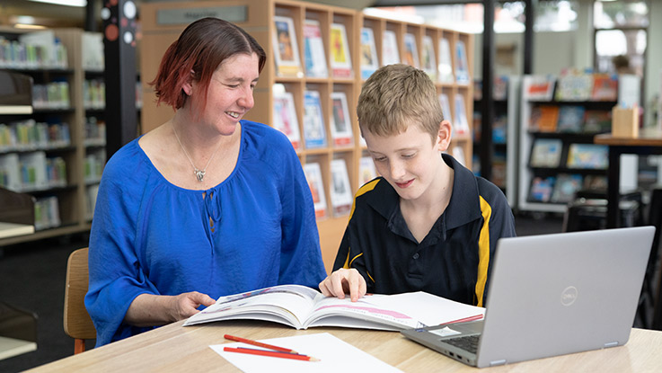 a mother sitting with her son in the library doing school work