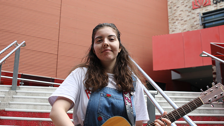 a girl with her guitar standing in front of a flight of stairs