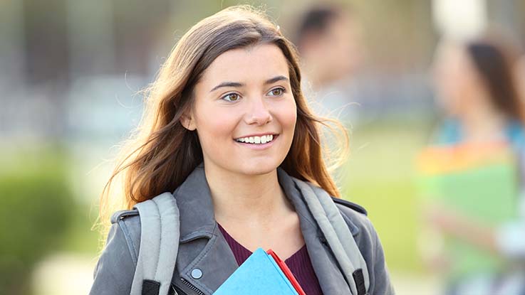 a woman carrying a backpack and holding book smiling