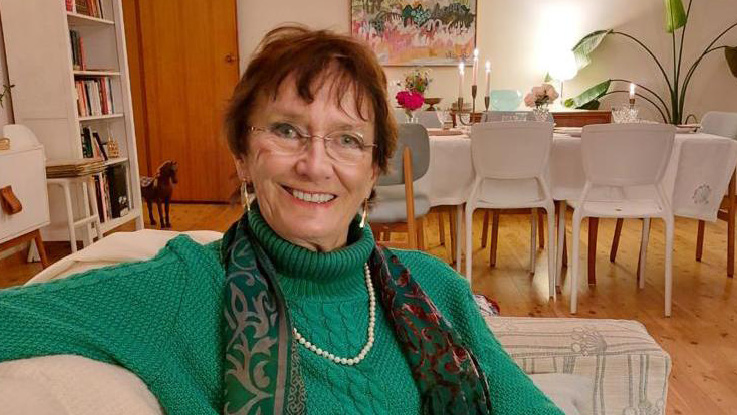a lady wearing a green woollen jumper sitting on the couch smiling