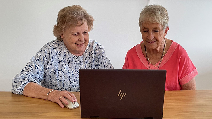 two ladies sitting in front of a laptop