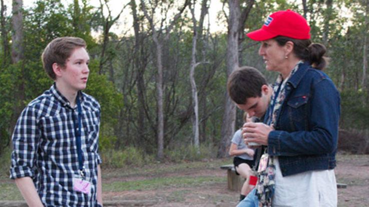 A boy talking to a woman whos wearing a red cap in a park