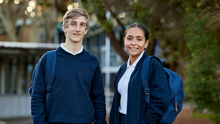 two students in blue school uniform in  a school playground with backpacks