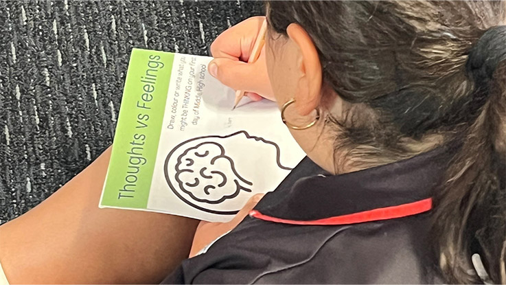 a student is writing on a worksheet that is labelled thoughts and feelings