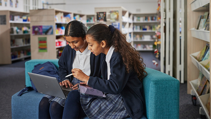 two school girls on a laptop working together in a library