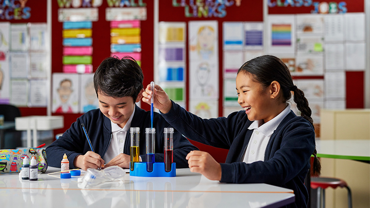 two school kids in a classroom doing a science project